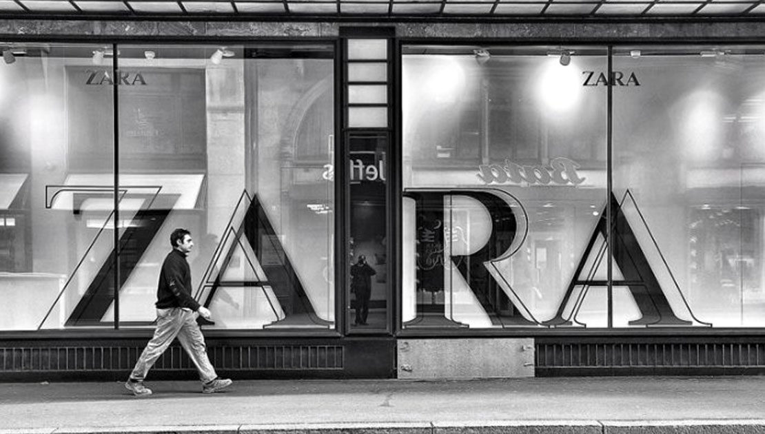 uomo passeggia davanti vetrina negozio Zara con grande insegna
