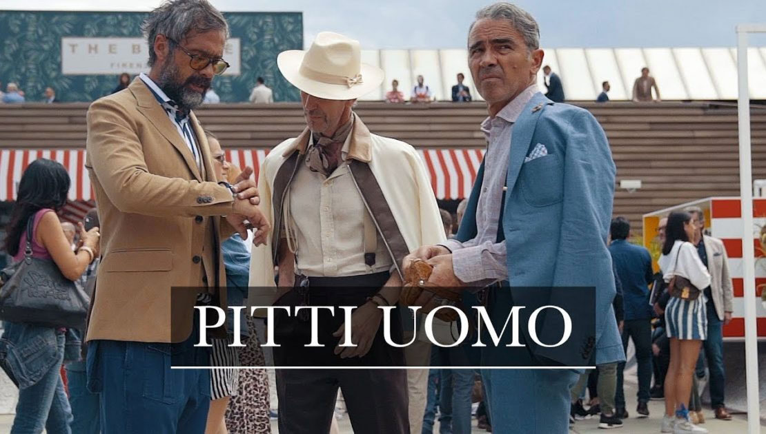 Scritta Marchio Pitti Uomo con tre uomini vestiti d'alta moda e sfondo di fiera